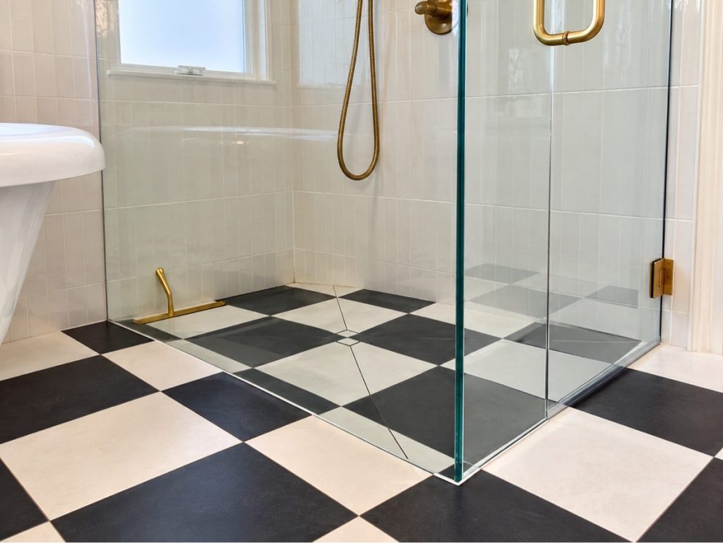 Curbless shower floor with black and white checkerboard tile flowing level from the bathroom floor